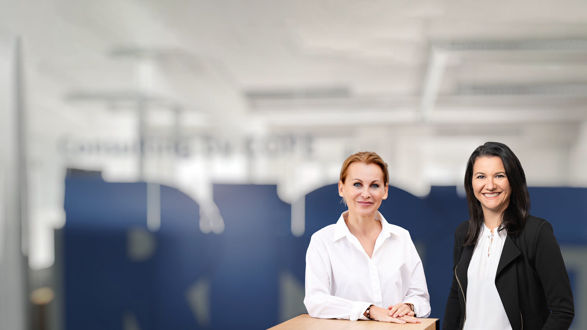 Gruppenbild der Geschäftsführerinnen der COPE Content Performance Group, Eva Maria Kubin und Marion Stelzer-Zöchbauer im Büro Wien vor einer Glaswand.
