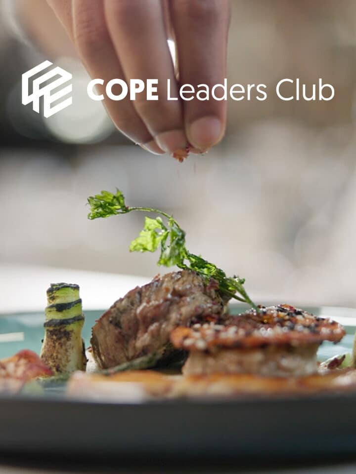 Eine Hand streut Gewürze auf ein Gourmetgericht mit Gemüse, Fleisch und Beilagen auf einem Teller; in der Ecke ist das Logo des COPE Leaders Club zu sehen.