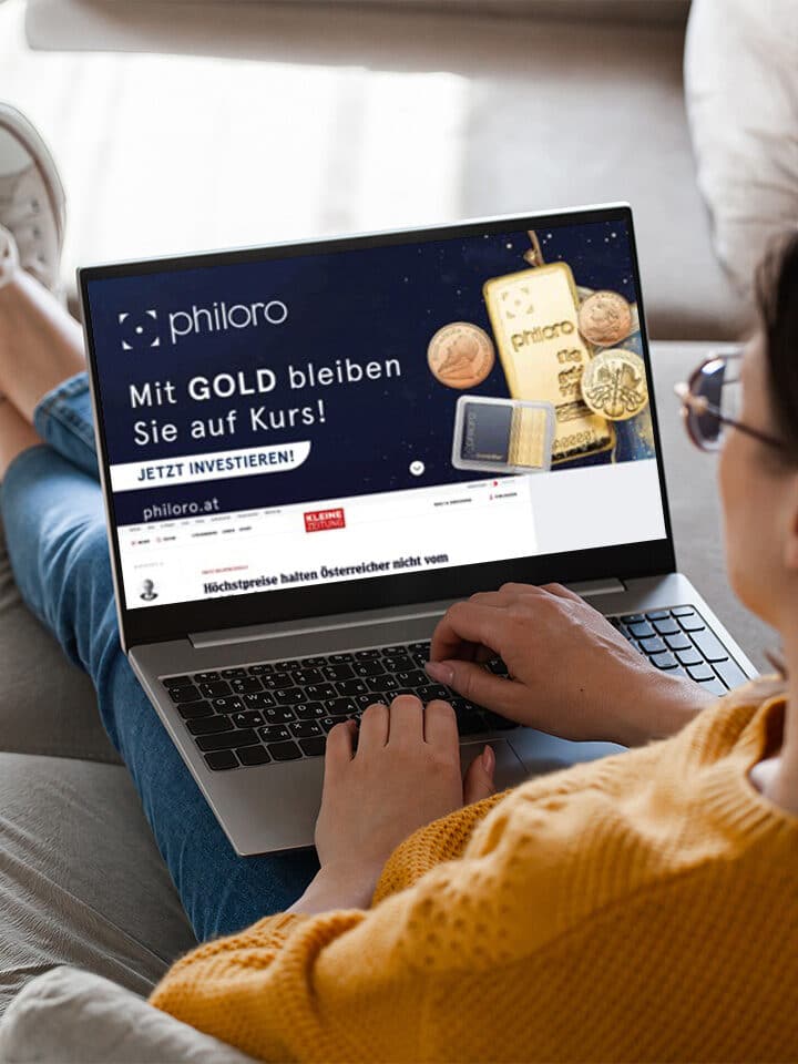 Eine Person, die auf einer Couch sitzt, benutzt einen Laptop, auf dem eine philoro-Website mit einer Werbung für deutsche Goldanlagen angezeigt wird.
